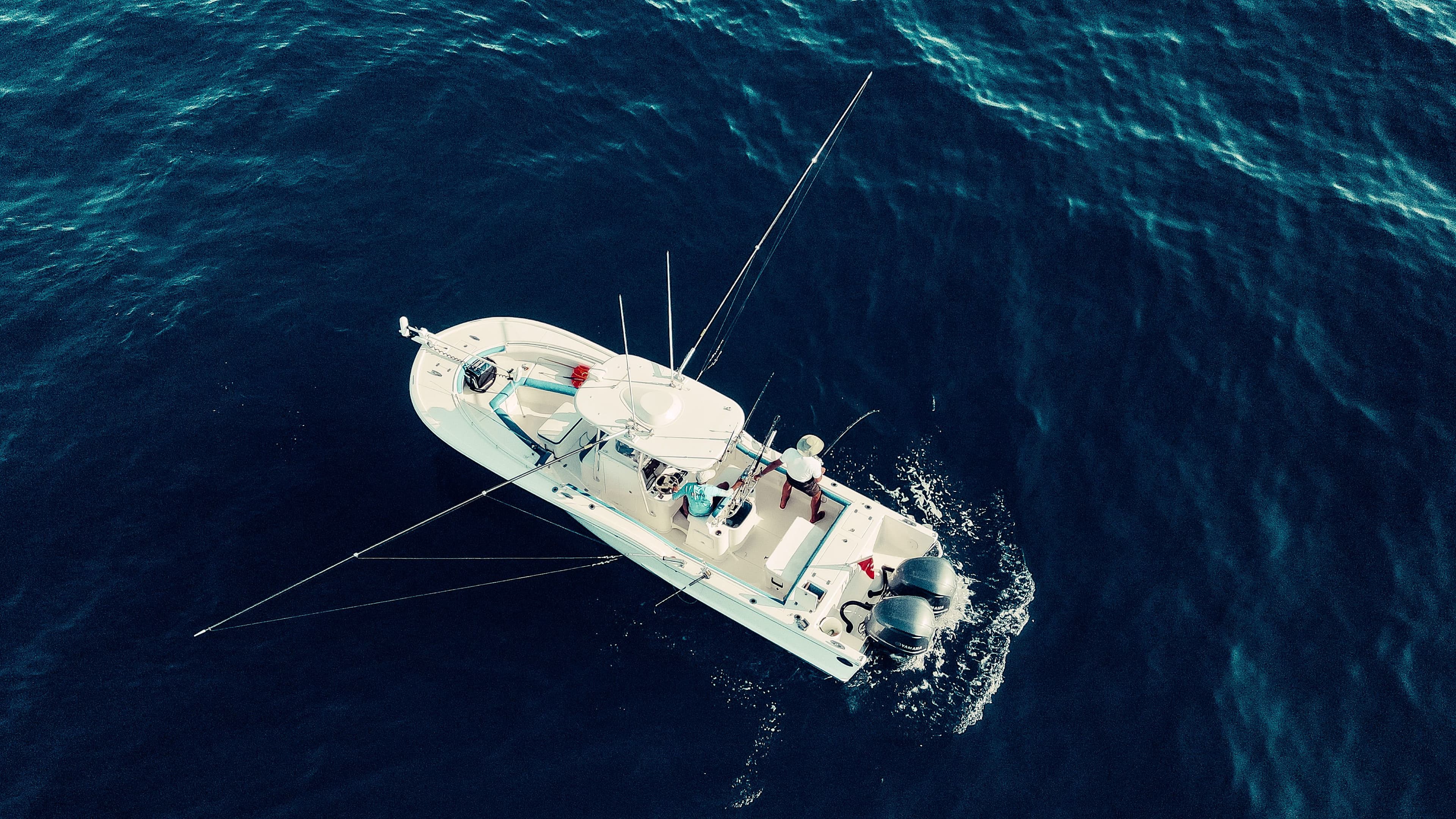Aerial view of a white fishing boat cruising through deep blue water
